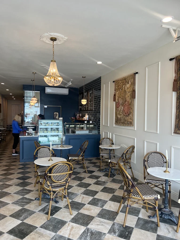 The navy pastry and gelato counter at Creperie Antoinette under brass pendants, with marble bistro tables on the checkered floor