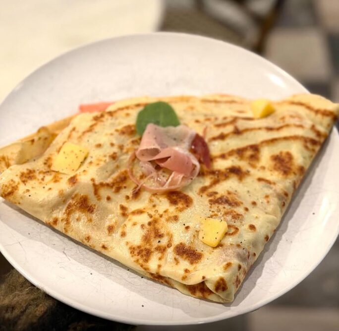 A folded ham and cheese crêpe on a white plate