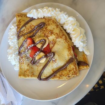 A folded crêpe with Nutella drizzle, fresh strawberries and whipped cream on a white plate