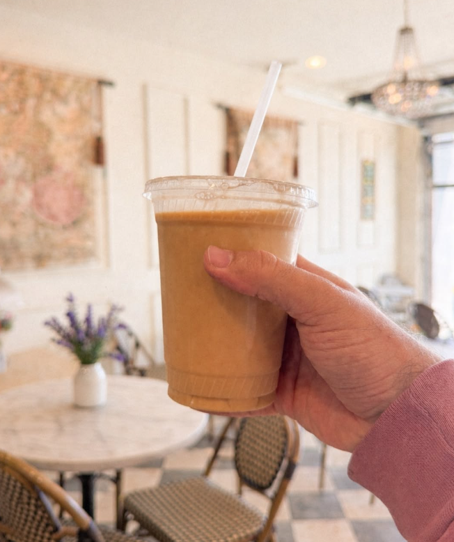 A hand holding a blended smoothie in a clear cup inside Creperie Antoinette