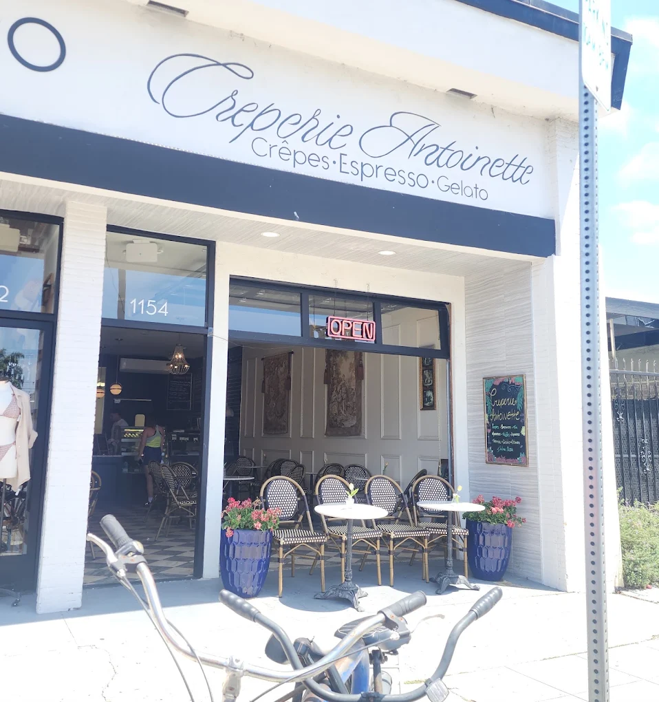 The Creperie Antoinette storefront on Garnet Avenue with sidewalk bistro tables, flower planters and the neon open sign